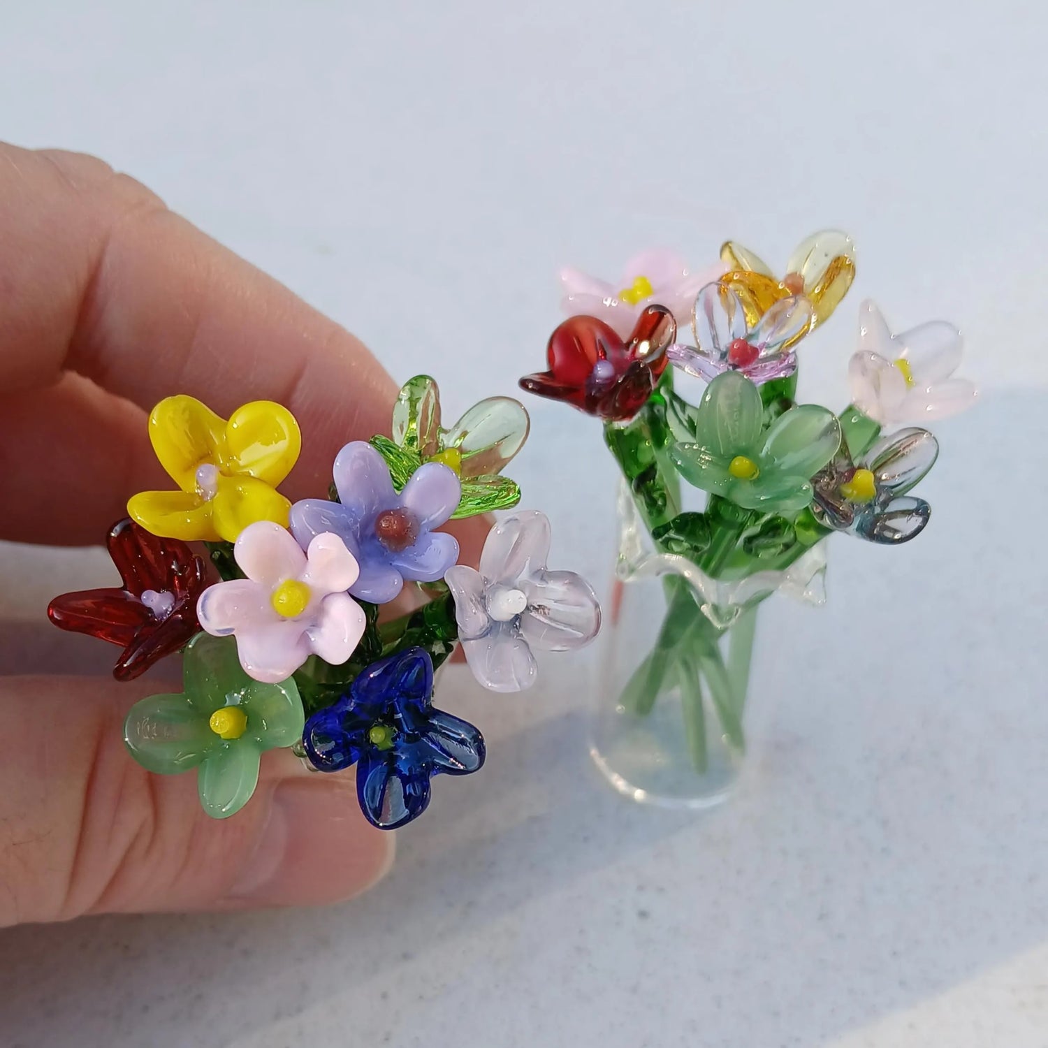 Close up of mini glass flowers in a vase with another vase in the background.

