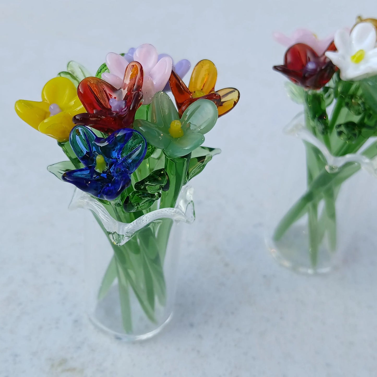 Two miniature glass vases with multicolored handmade lampwork flowers displayed side by side