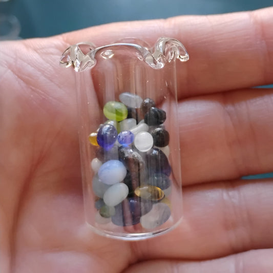 Small transparent container filled with multicolored stones held in a hand.